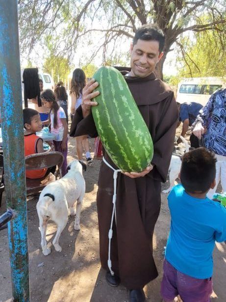 A man in a brown robe is holding a large watermelon