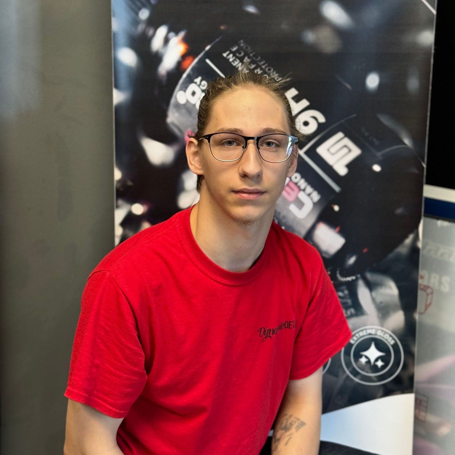 A young man wearing glasses and a red shirt is sitting in front of a sign that says ' g ' on it