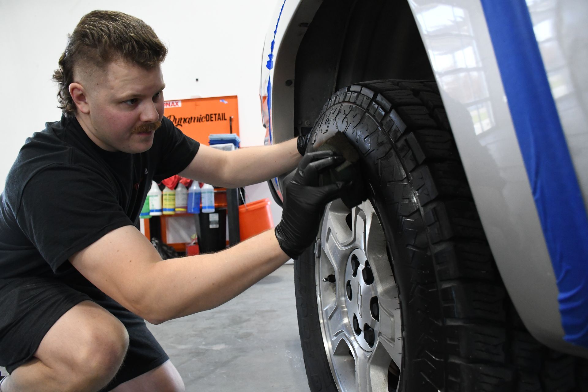 A man is kneeling down and cleaning a tire on a car.