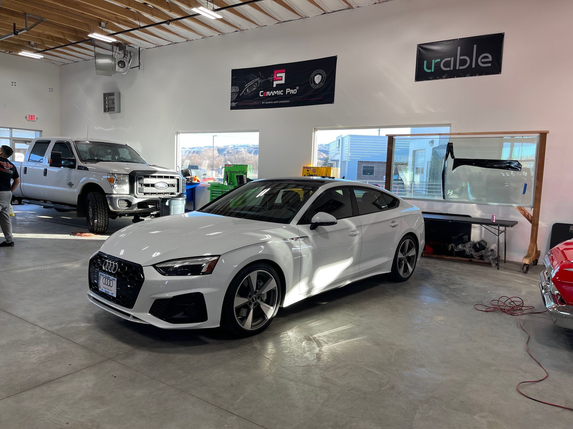 A white car is parked in a garage next to a truck.