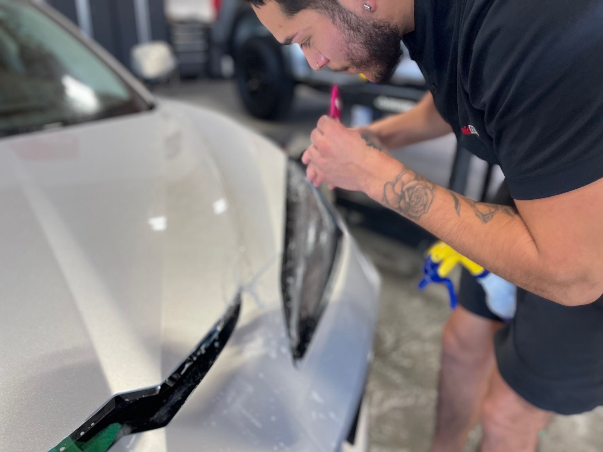 A man is cleaning the front of a silver car