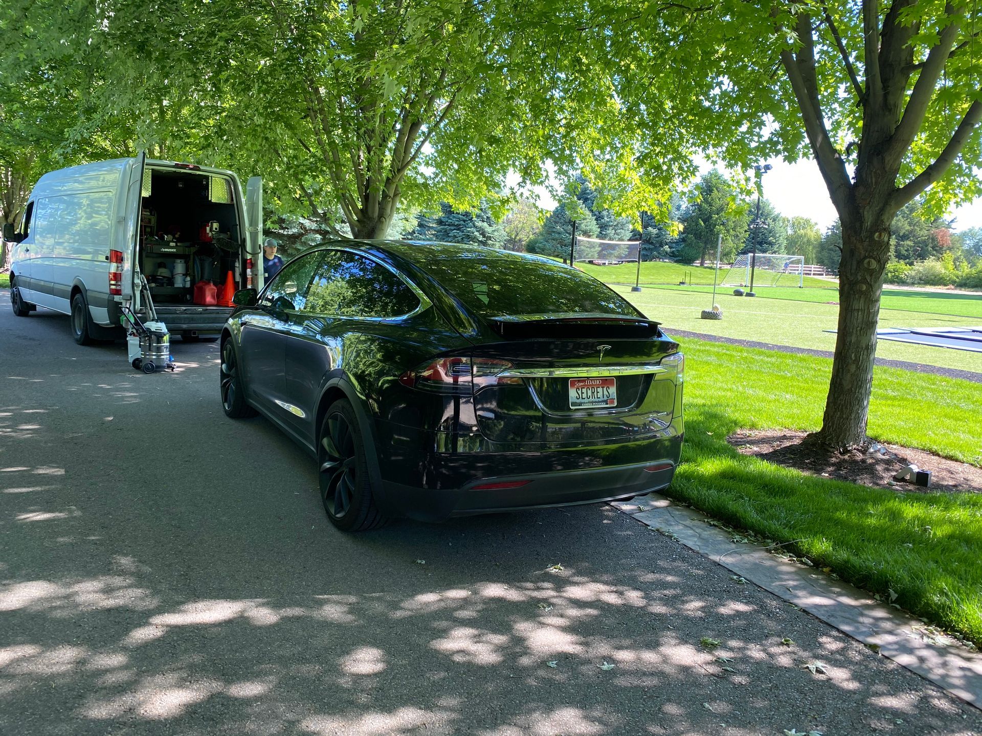 A black tesla model x is parked on the side of the road next to a white van.