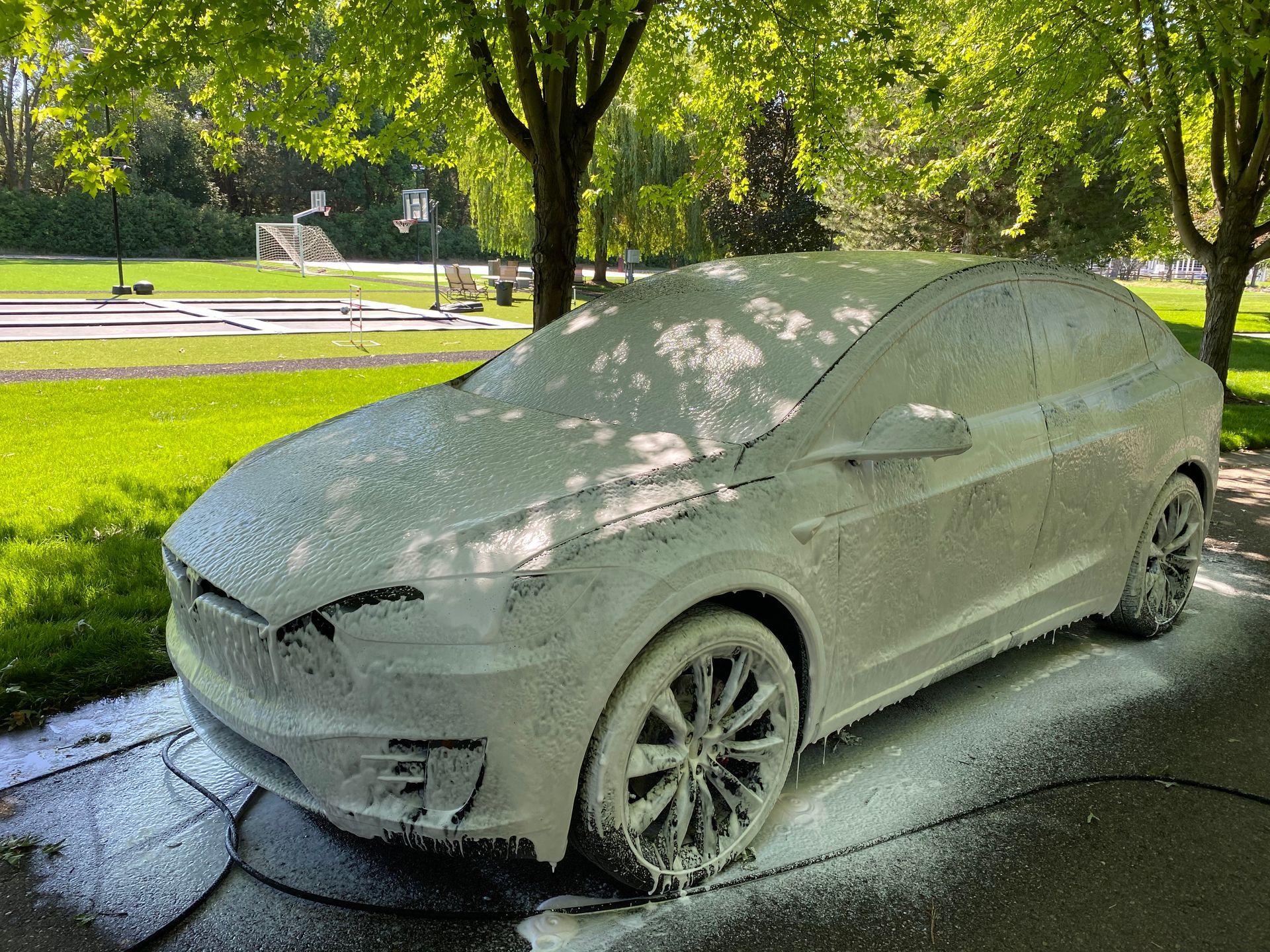 A tesla model x is covered in foam in a driveway.