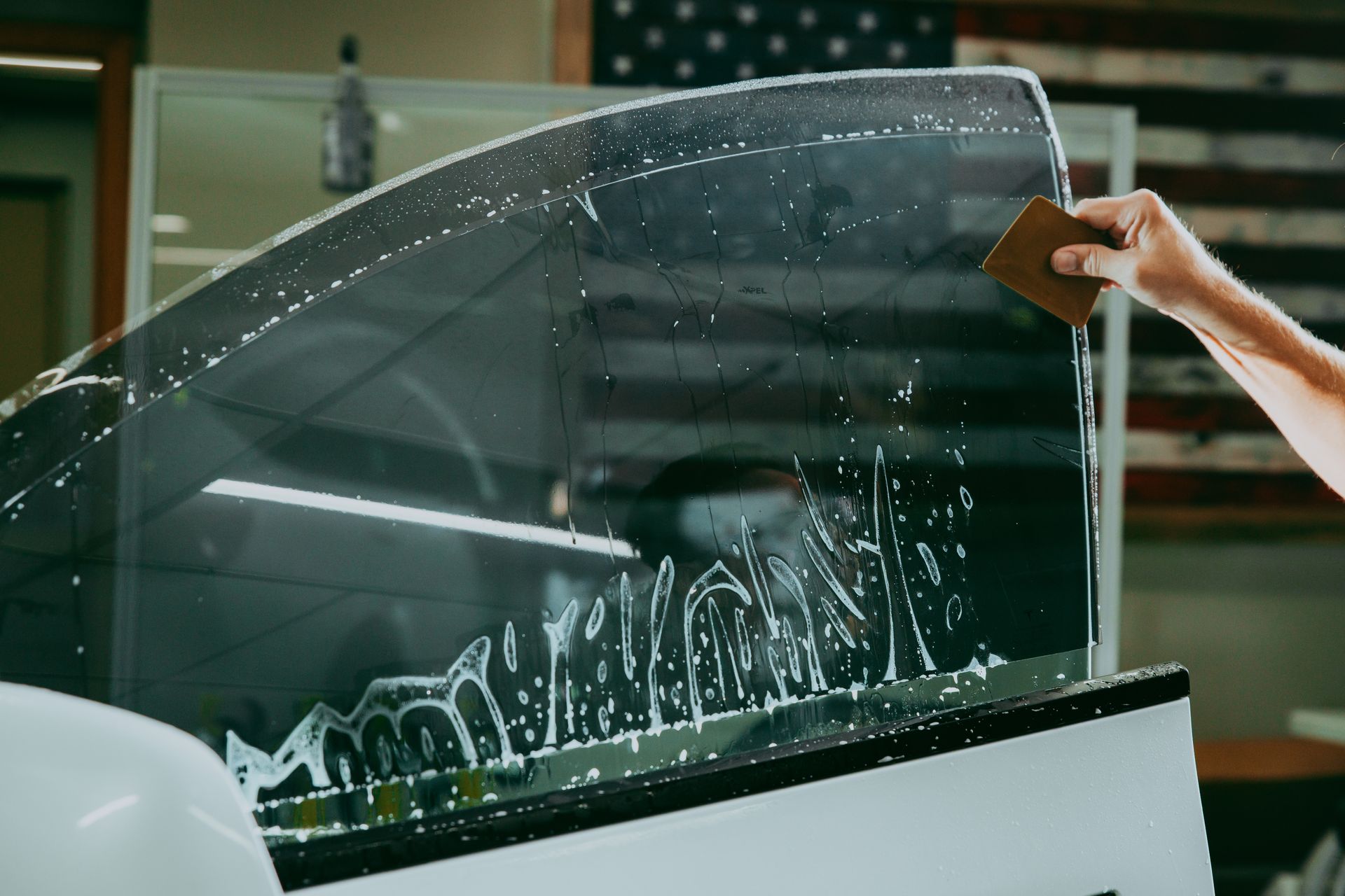 A person is applying tinted window film to a car window.