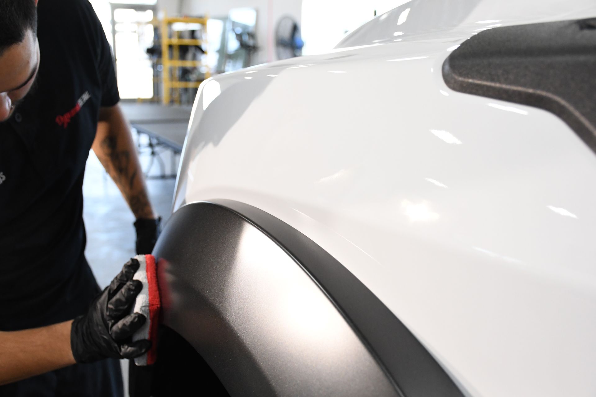 A man is polishing the fender of a white car.