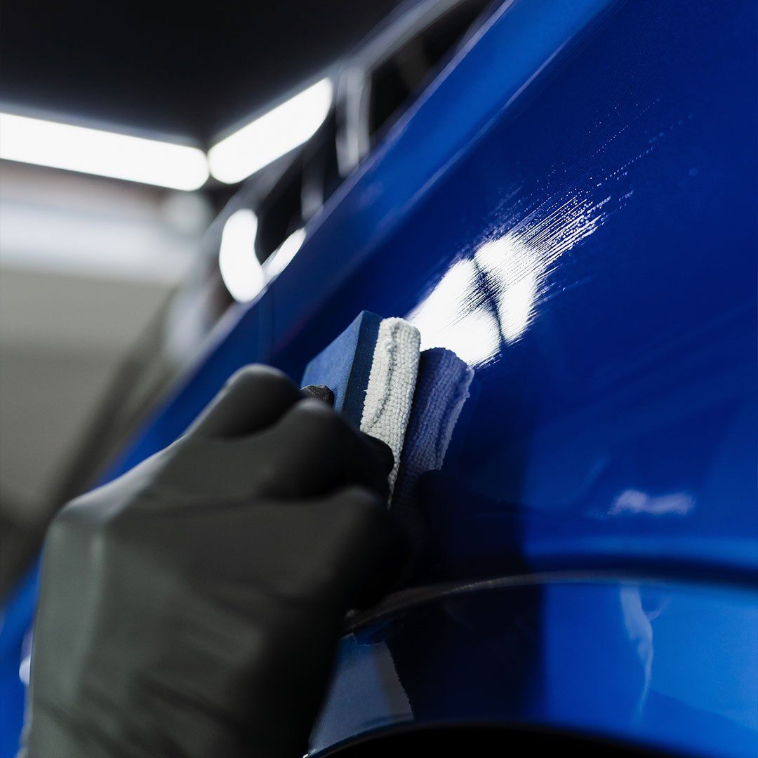 A person is polishing a blue car with a sponge.