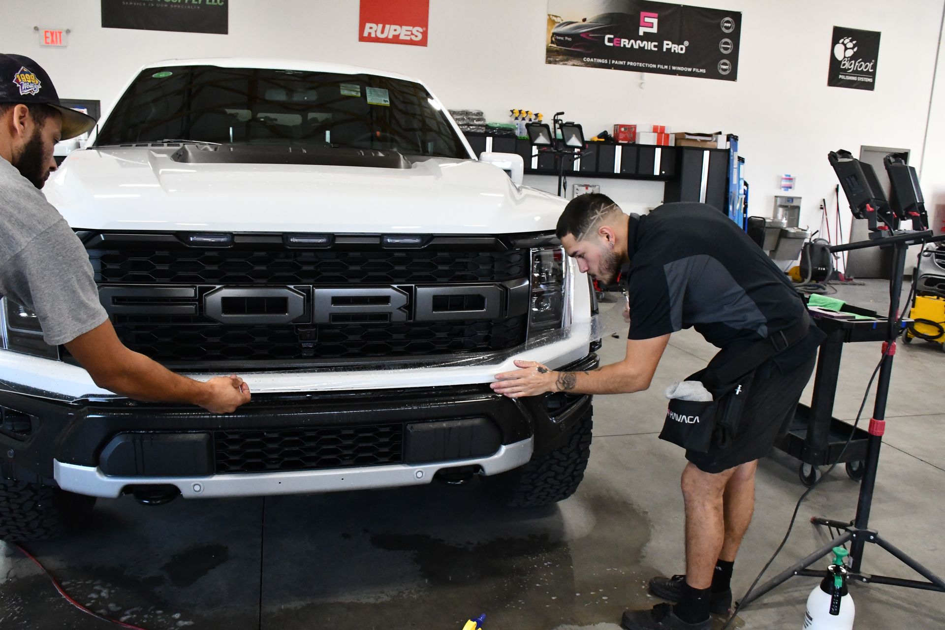 Two men are working on a white ford truck in a garage.
