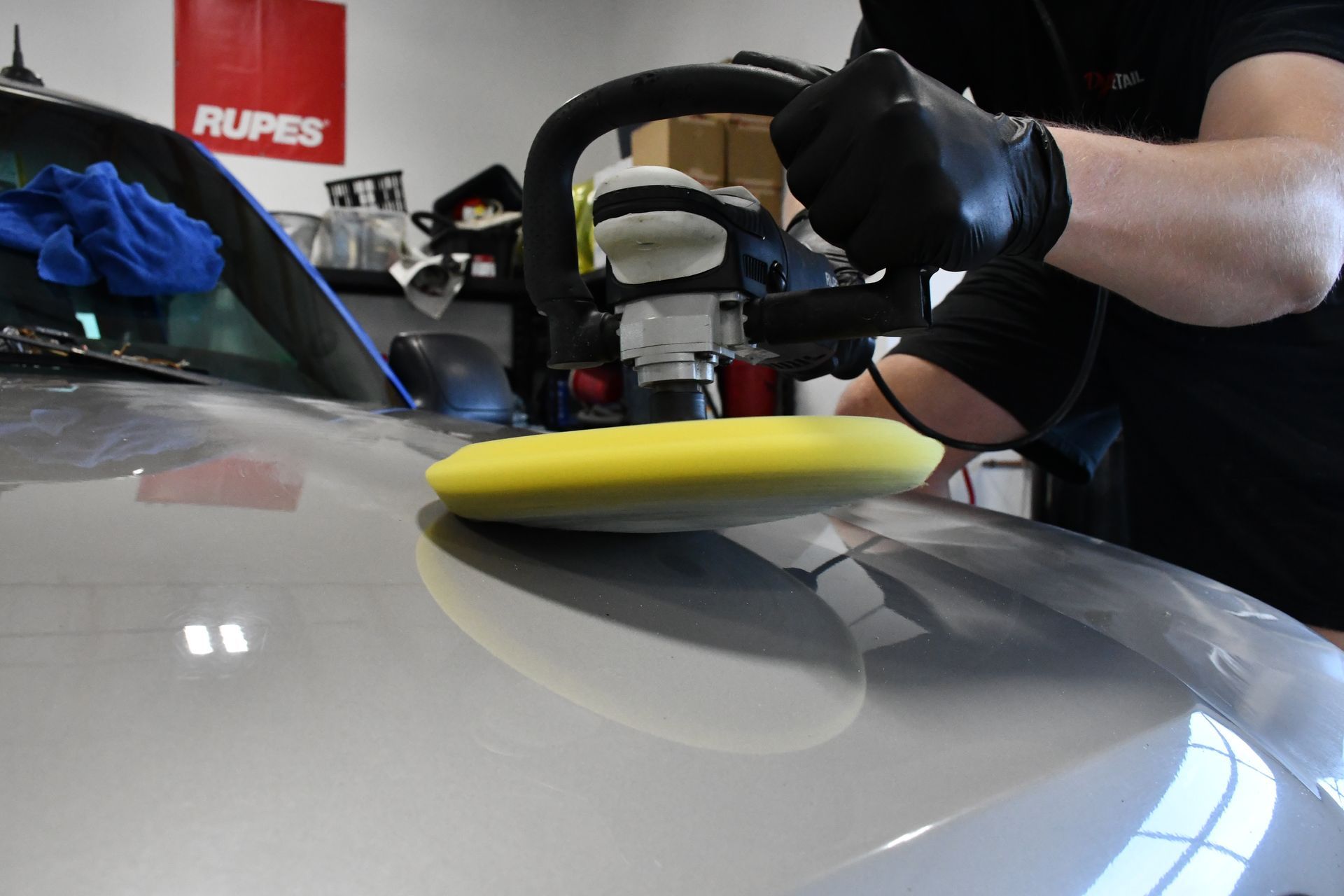 A man is polishing the hood of a car with a yellow polishing pad.