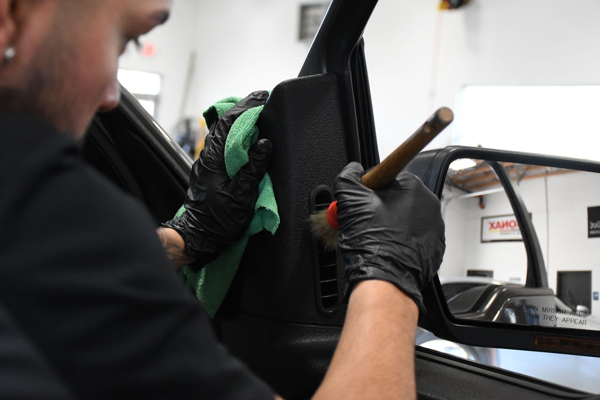 A man is cleaning a car door with a cloth and brush.