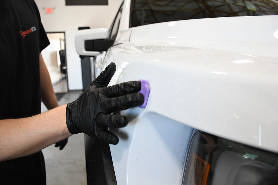 A person wearing black gloves is polishing a white car.