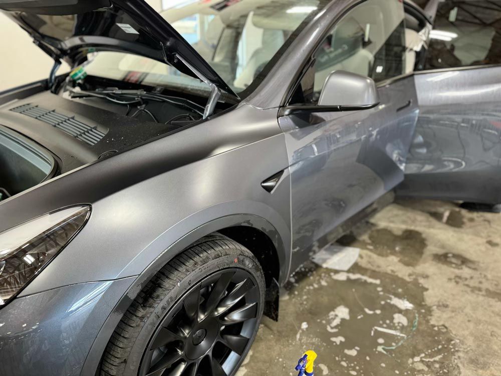 A tesla model y is parked in a garage with the hood up.