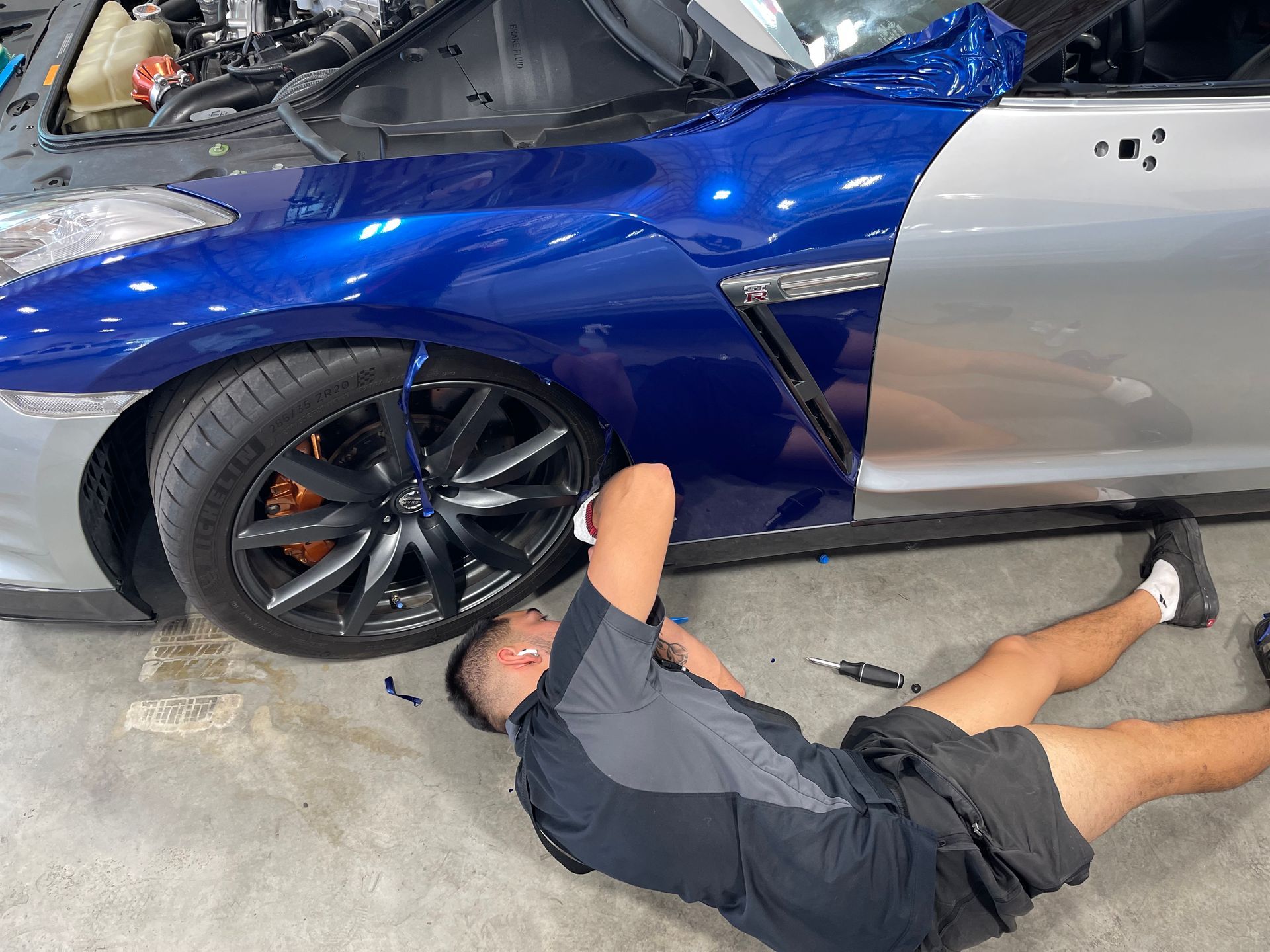 A man is laying on the ground working on a car.