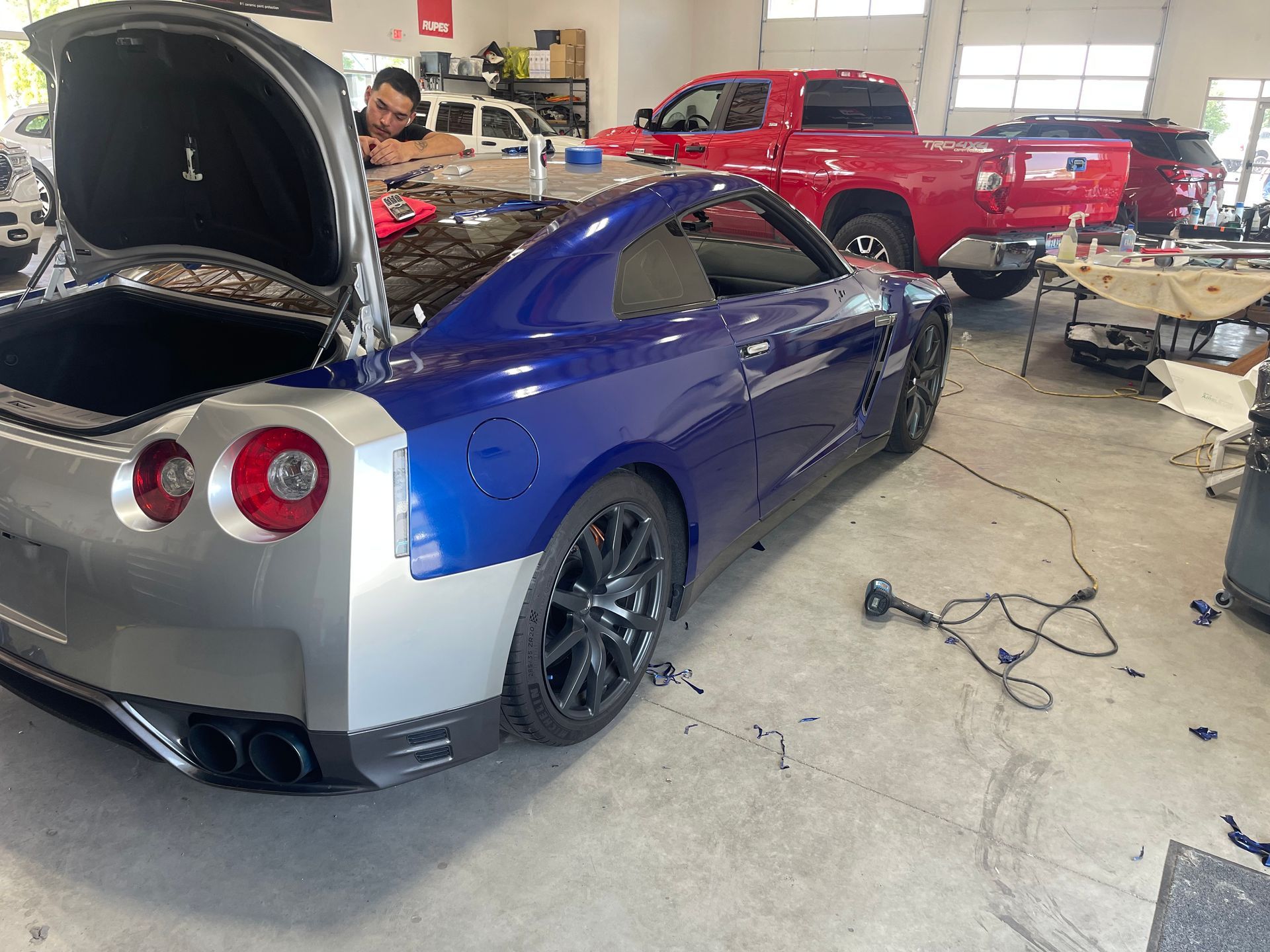 A blue sports car with the trunk open is in a garage.