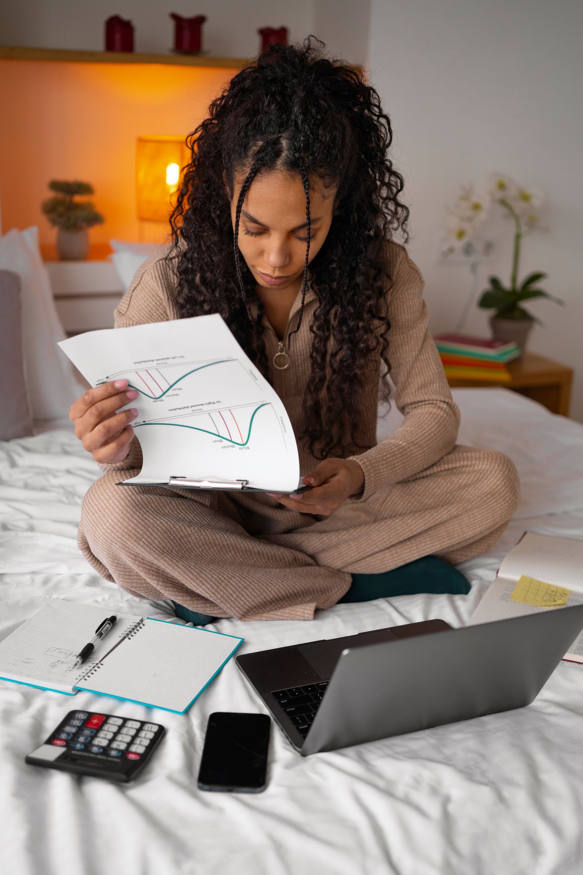 A woman is sitting on a bed with a laptop and a calculator.