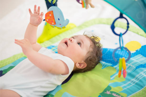 A baby is laying on a play mat playing with toys.