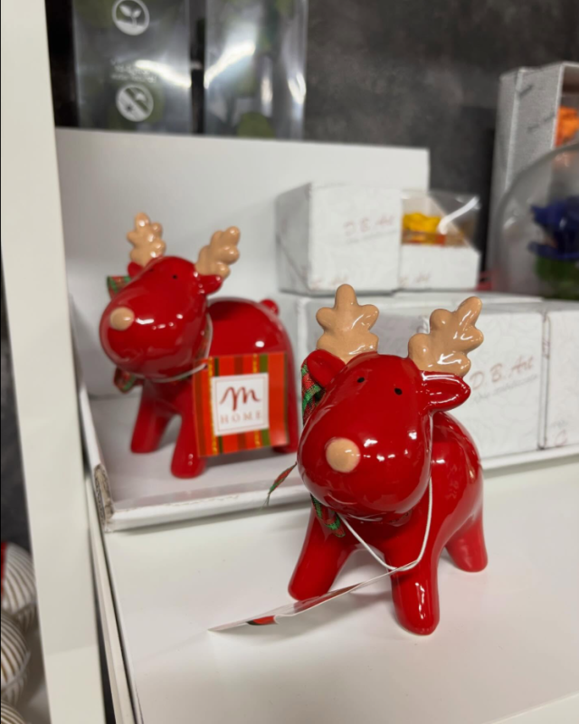 Due statuette di renne rosse con corna color cuoio e stringhe bianche su uno scaffale.