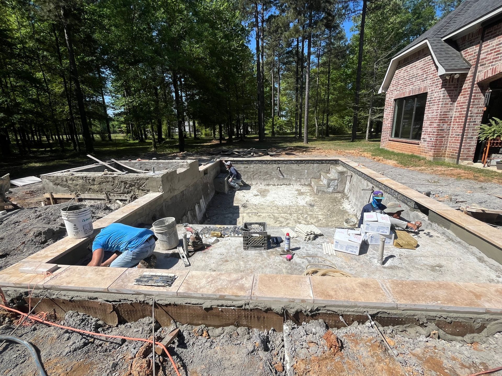 A man is working on a swimming pool in front of a brick house.