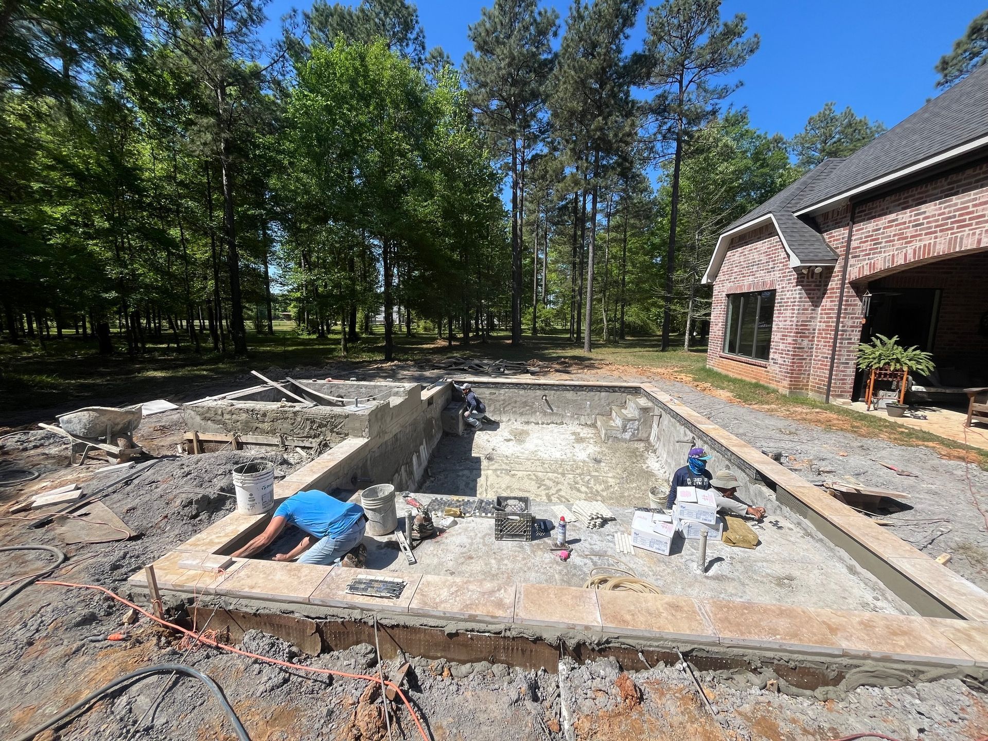 A man is laying in the dirt next to a swimming pool under construction.