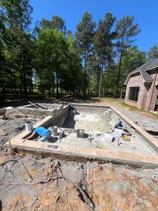 A man is laying on the ground next to a swimming pool under construction.