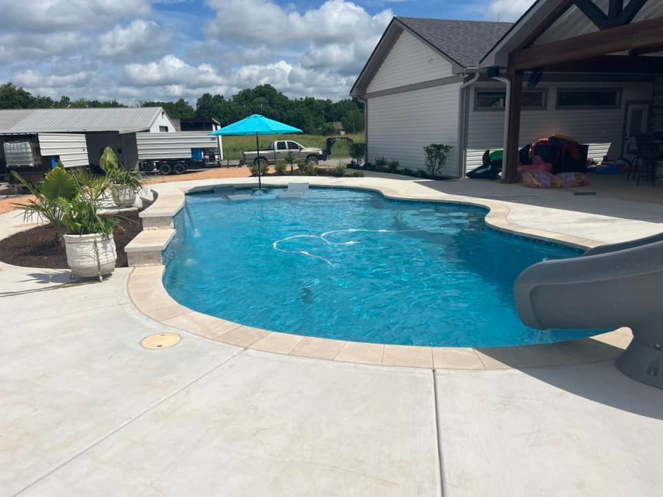 A large swimming pool with a slide and umbrella in front of a house.