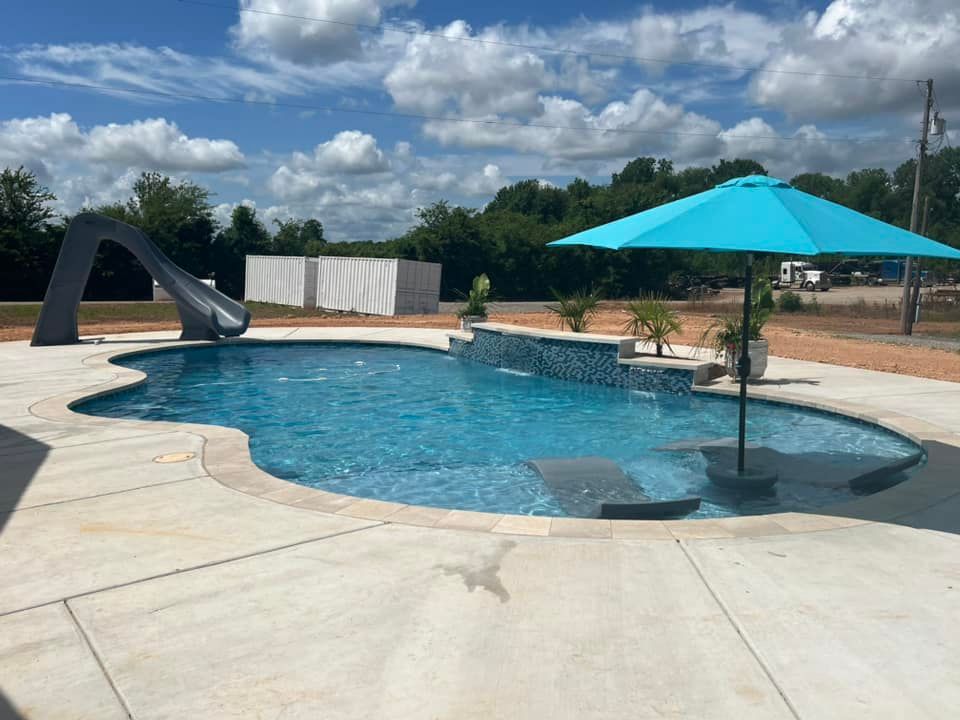 A large swimming pool with a blue umbrella and a slide.