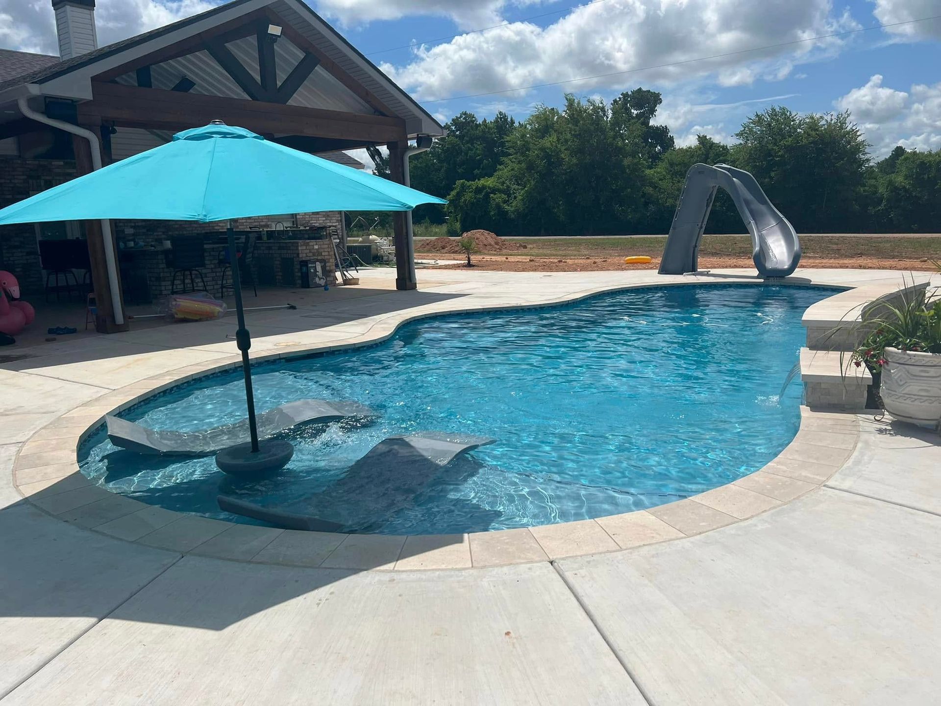 A large swimming pool with a blue umbrella and a slide.