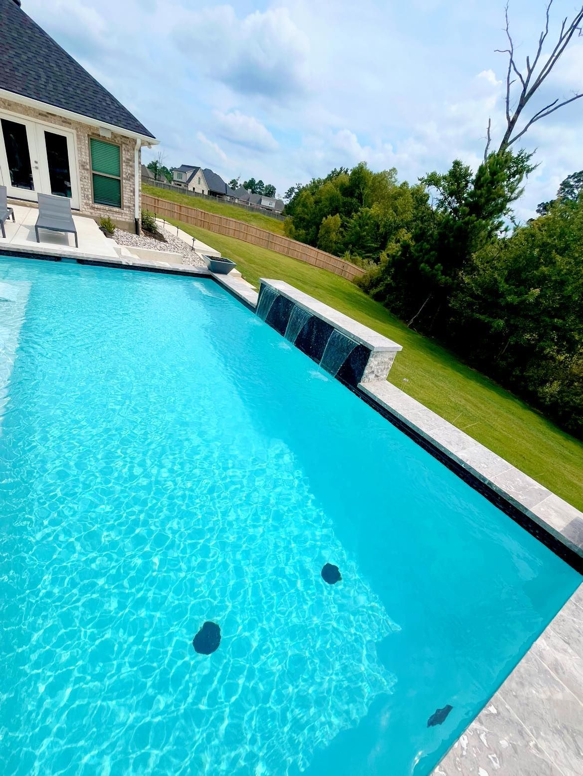 There is a large swimming pool in the backyard of a house.