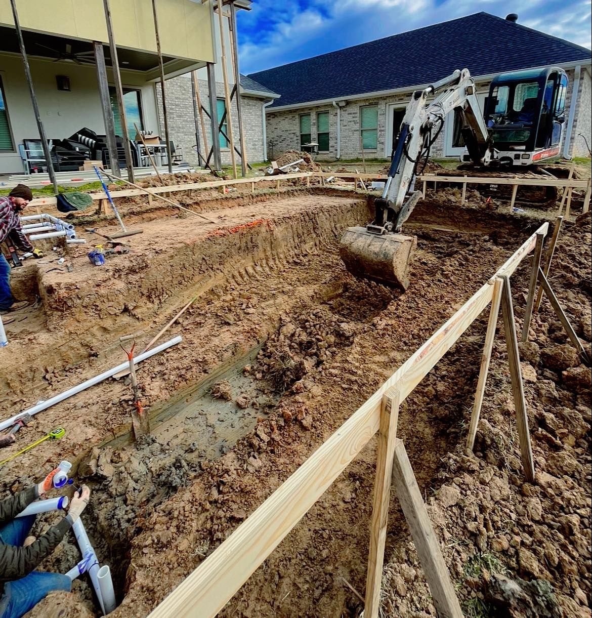 A man is digging a hole in the dirt in front of a house.
