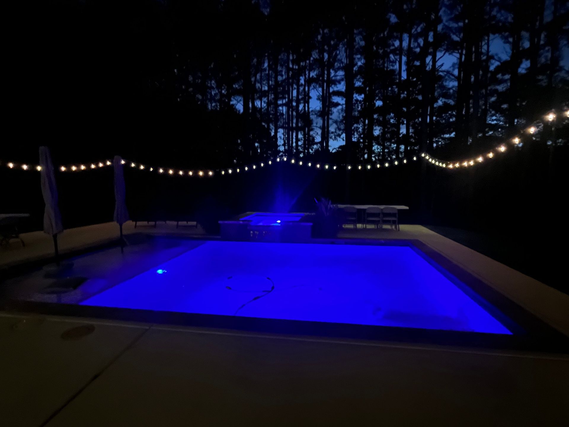 A large swimming pool is lit up at night with blue lights.