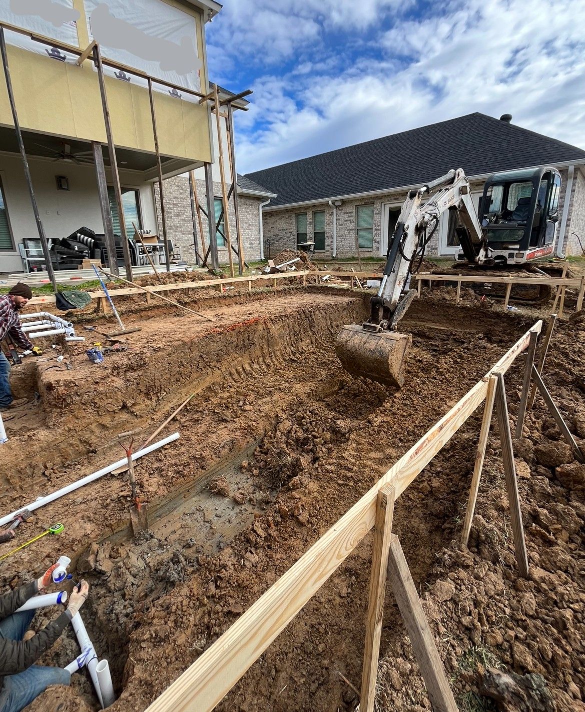 An excavator is digging a hole in the dirt in front of a house.