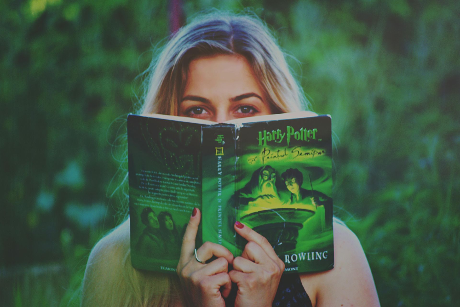 A woman is covering her face with a harry potter book.