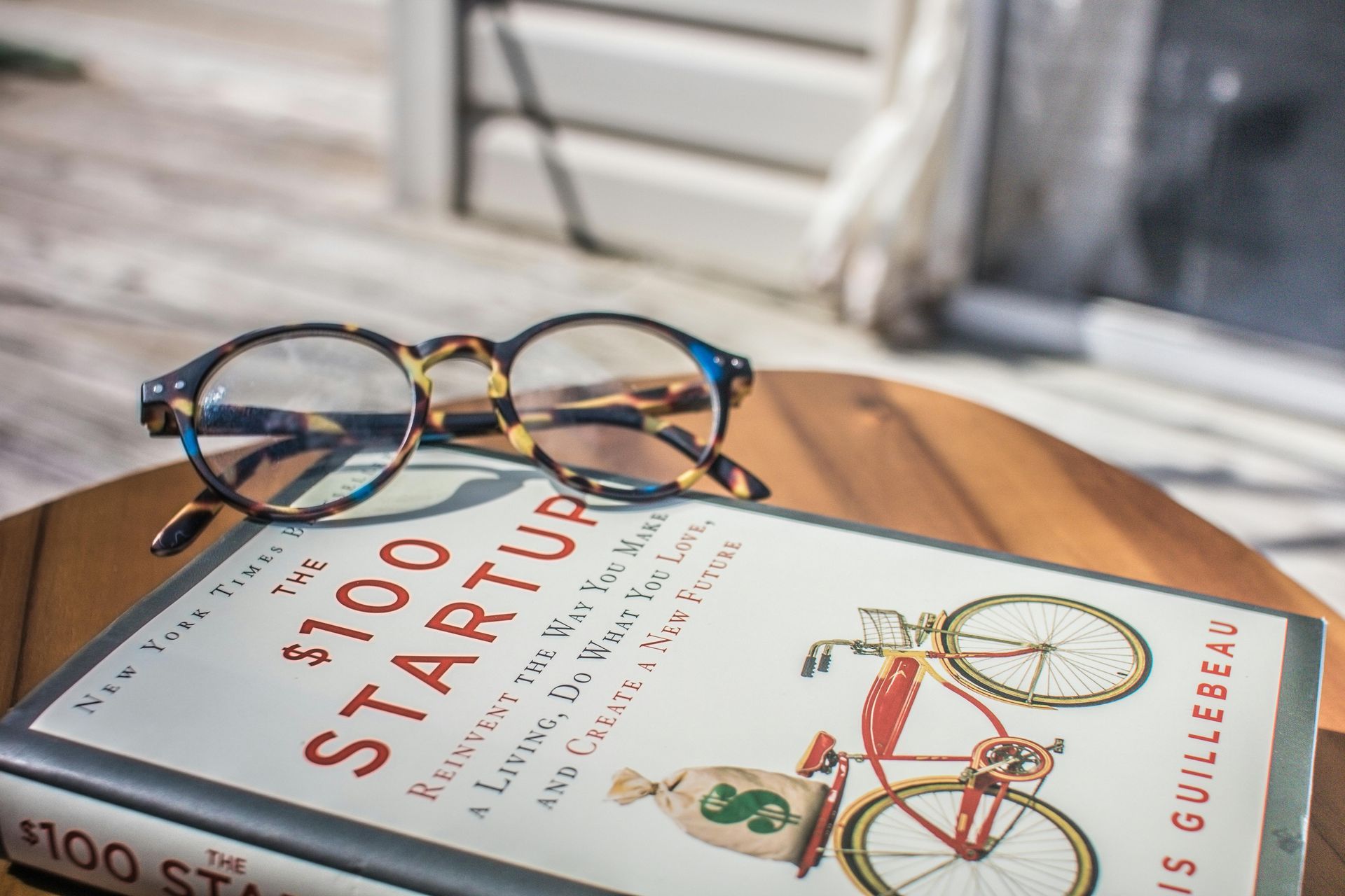 A pair of glasses is sitting on top of a $ 100 startup book.