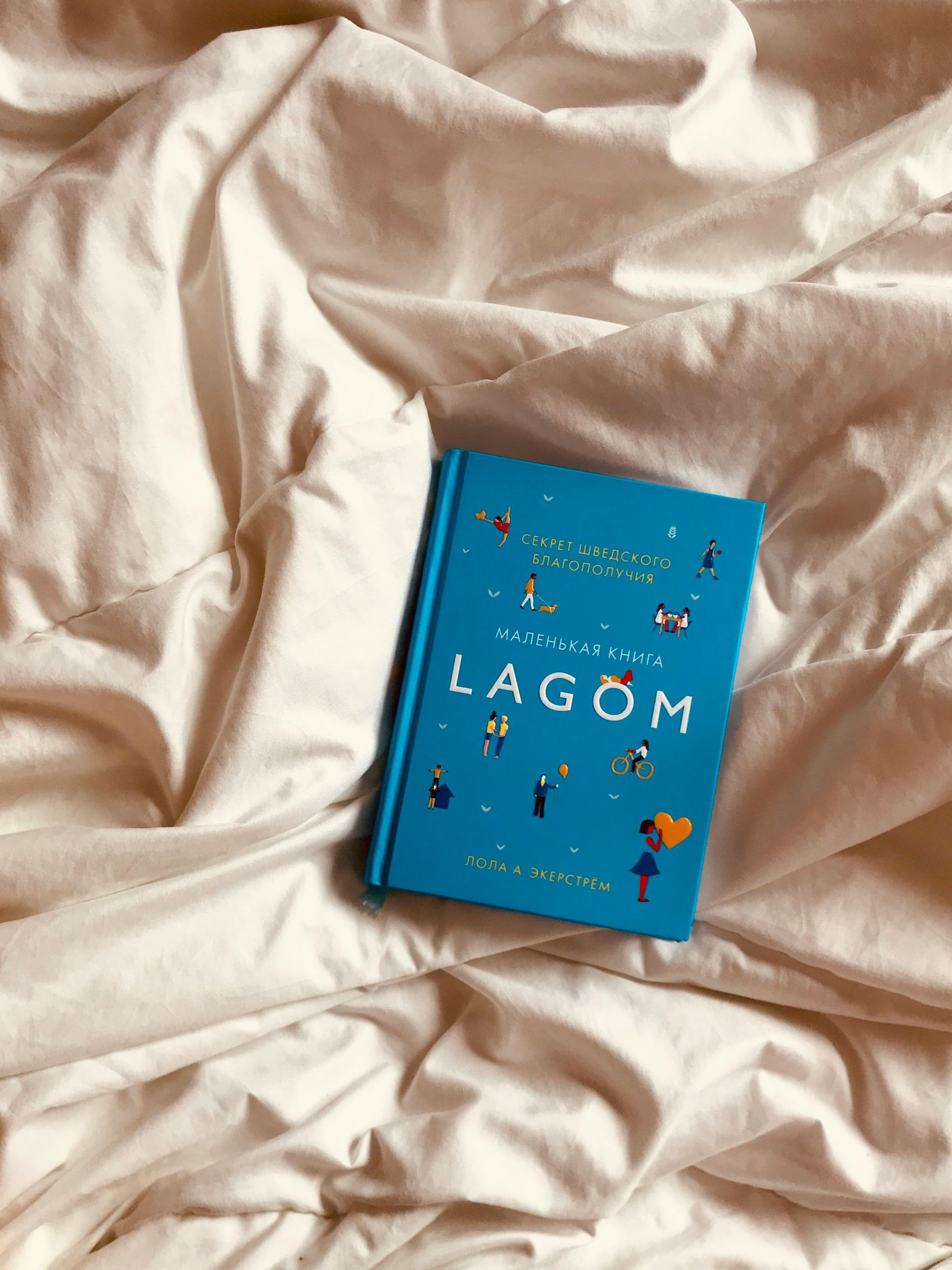 A blue book titled lagom is laying on a bed