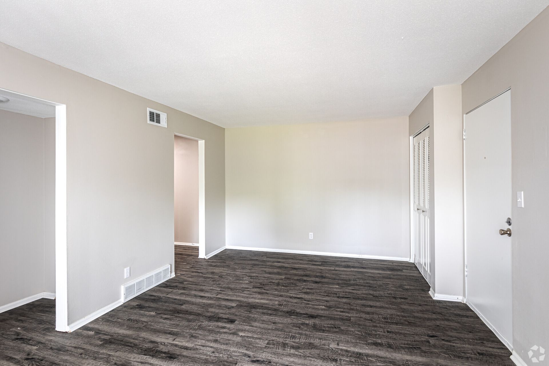 An empty living room with hardwood floors and white walls.