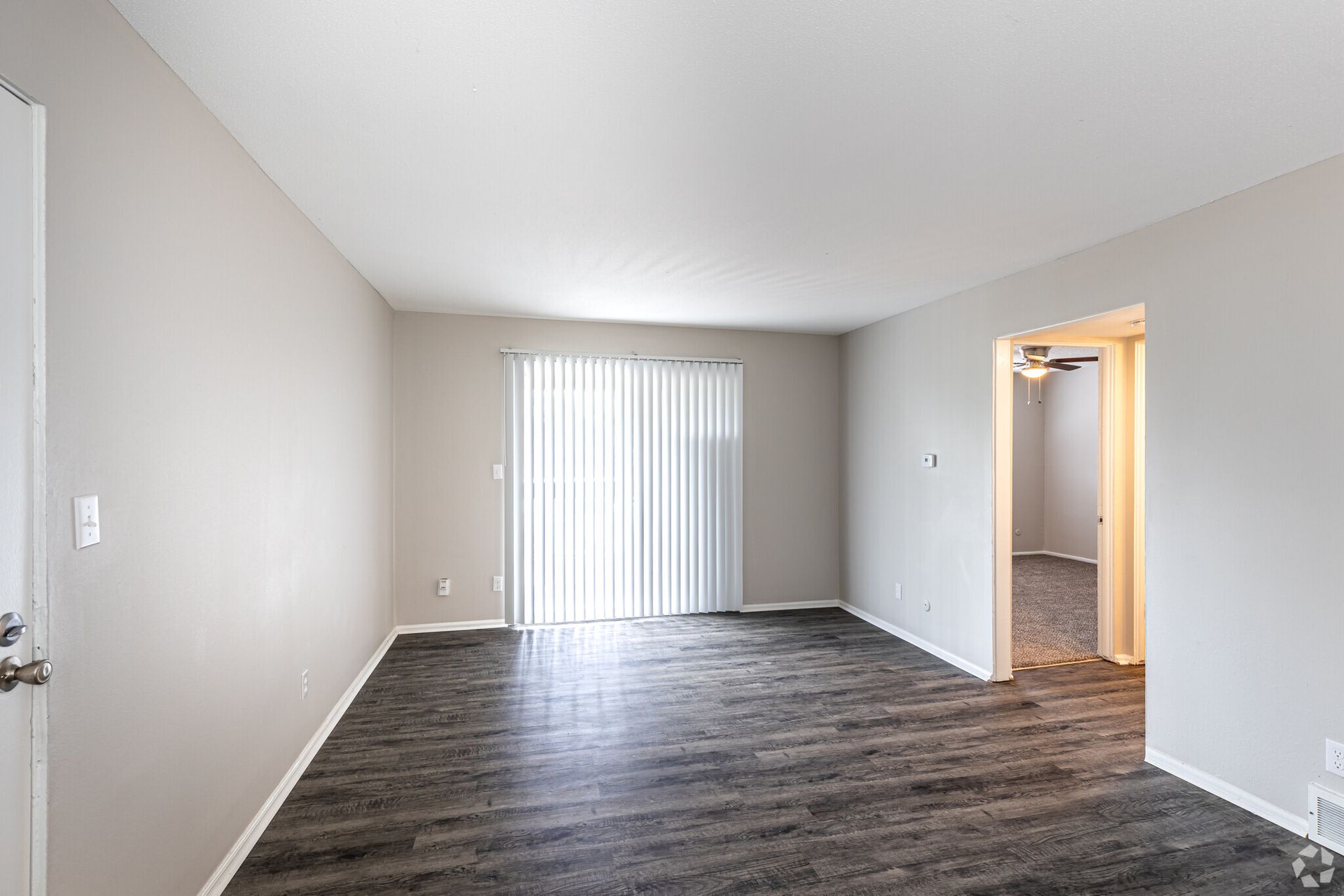 An empty living room with hardwood floors and a sliding glass door.