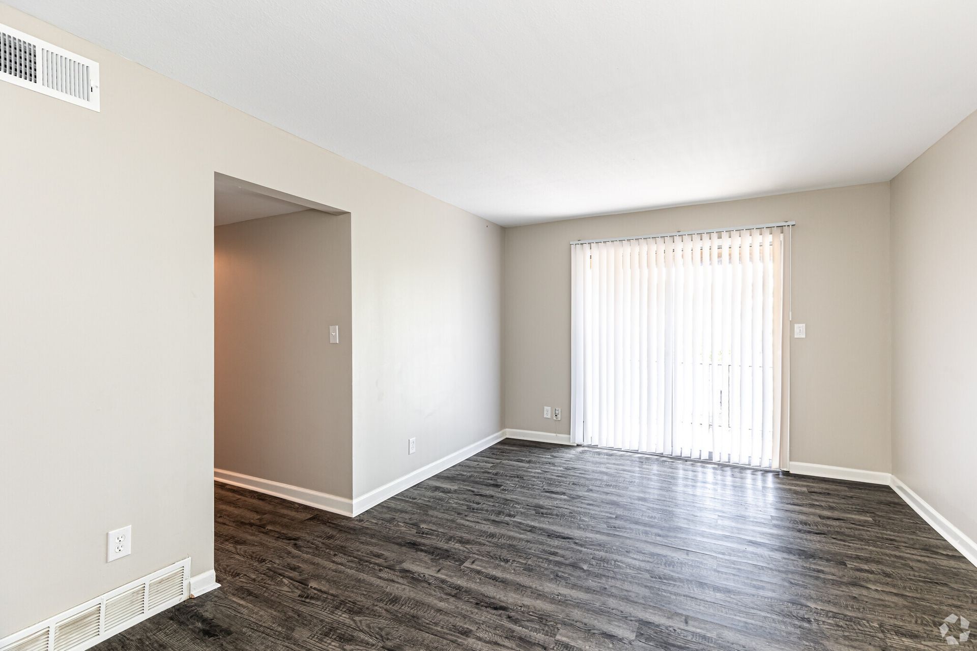 An empty living room with hardwood floors and a sliding glass door.