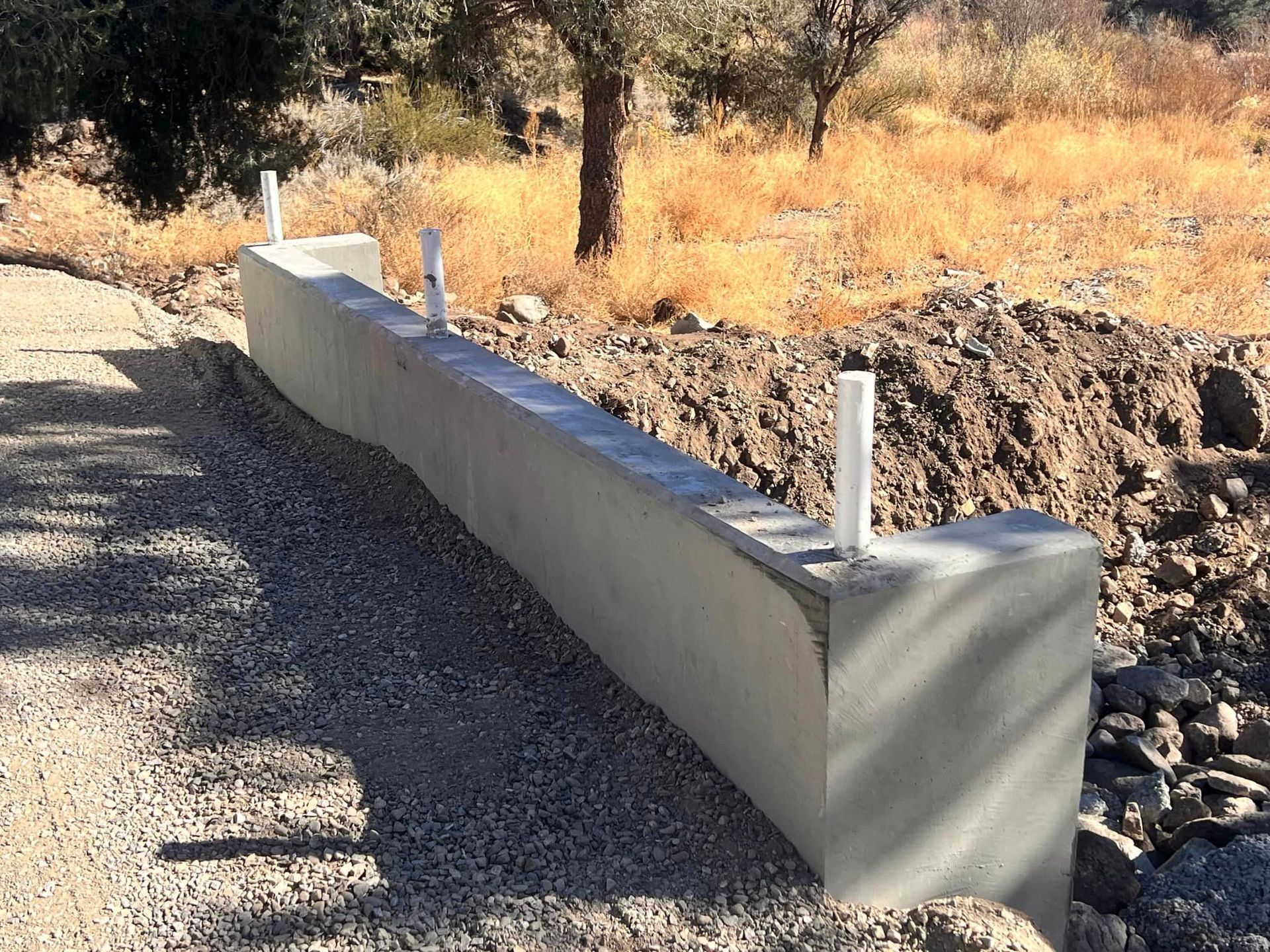 A concrete wall is sitting on the side of a gravel road