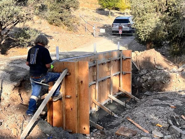 A man is standing next to a wooden wall in the dirt.