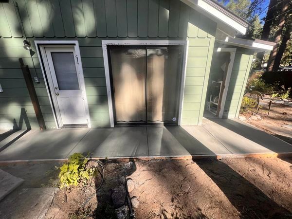 A green house with a white door and a concrete porch.
