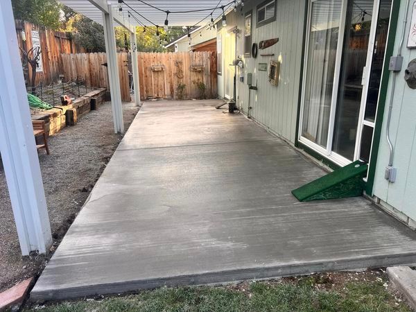 A concrete patio is being built in the backyard of a house.