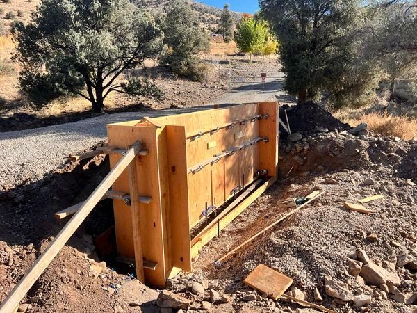 A wooden wall is being built in the dirt next to a road.