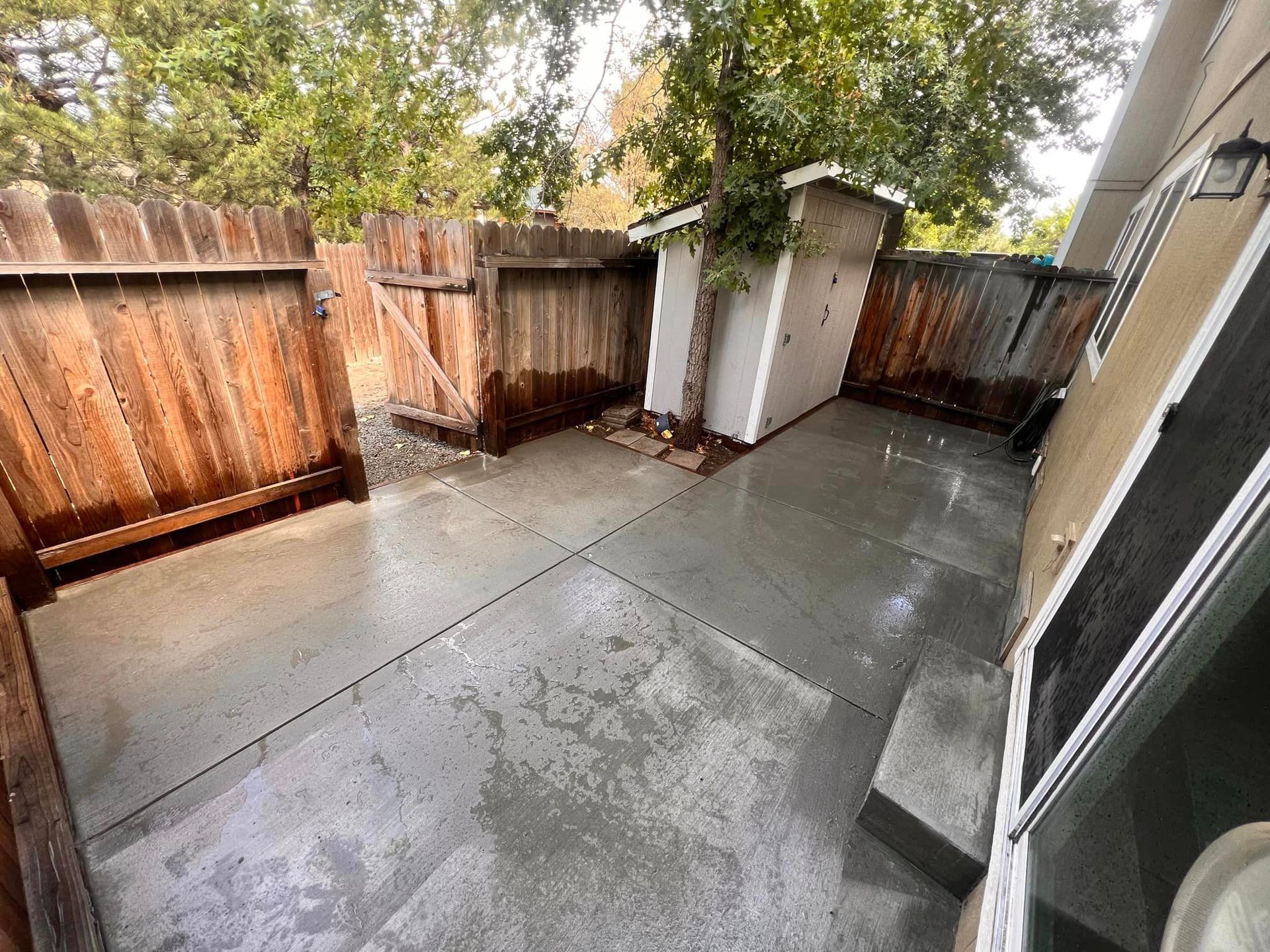 A patio with a wooden fence and a shed in the backyard of a house.