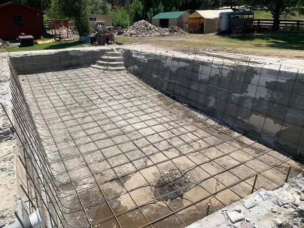 A swimming pool is being built in a yard with a tractor in the background.