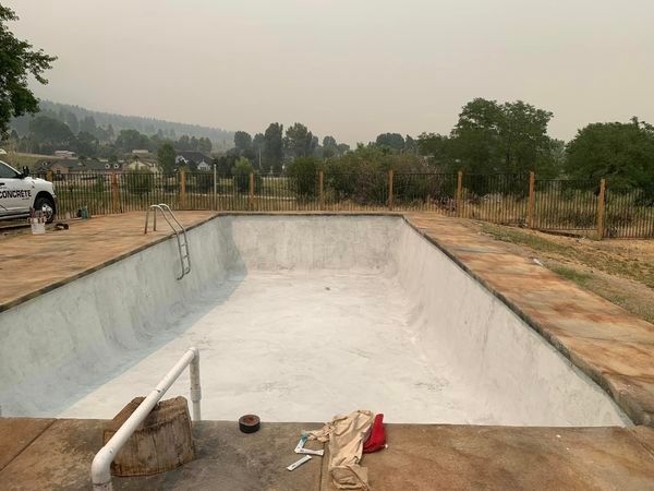 An empty swimming pool with a white car parked in the background.