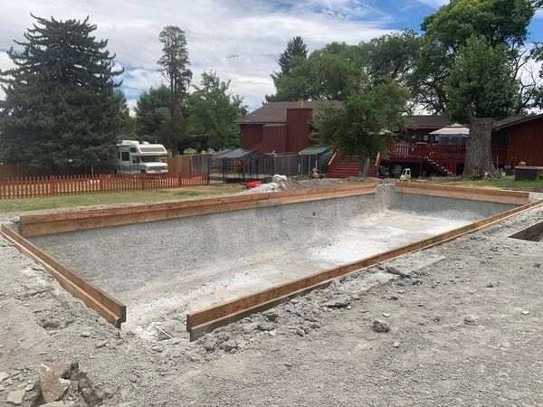 A large concrete pool is being built in the backyard of a house.