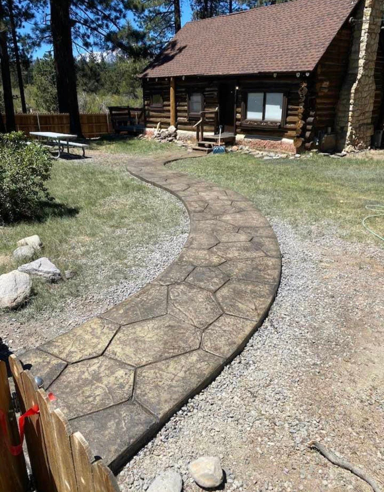 A stone walkway leading to a log cabin in the woods.