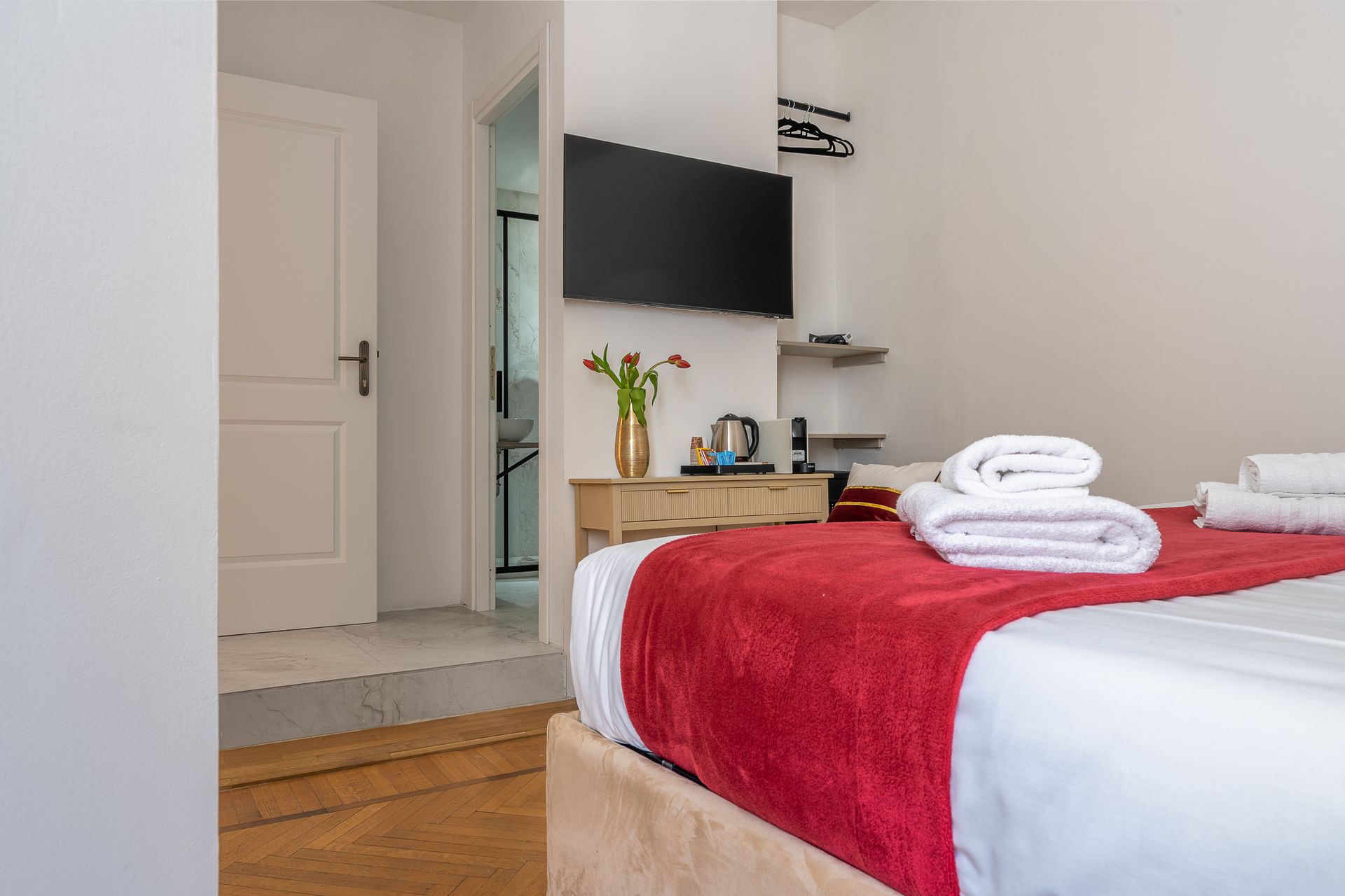 There is a bed with a red blanket and towels on it in a hotel room.