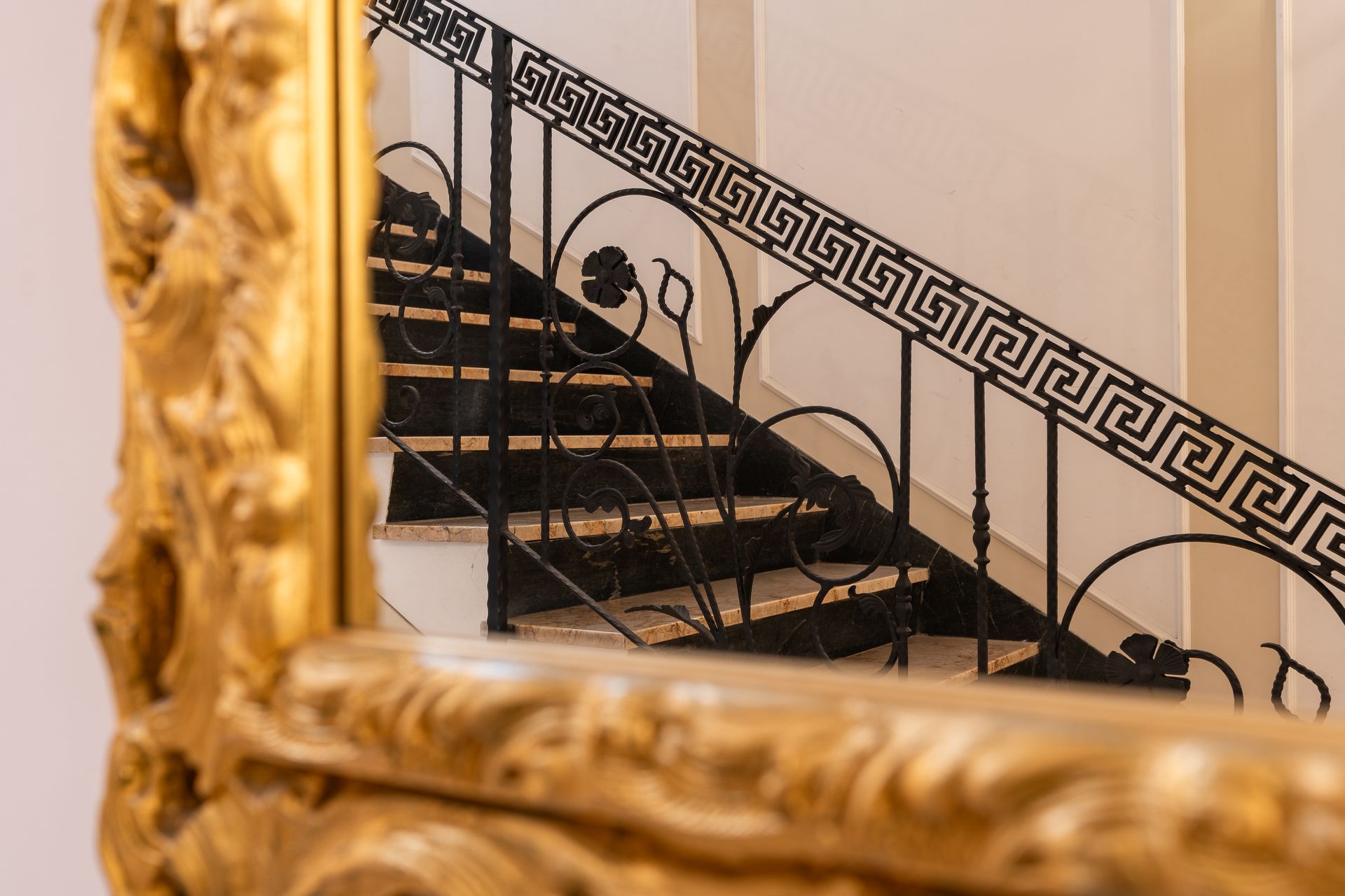 A staircase with a wrought iron railing is reflected in a mirror.