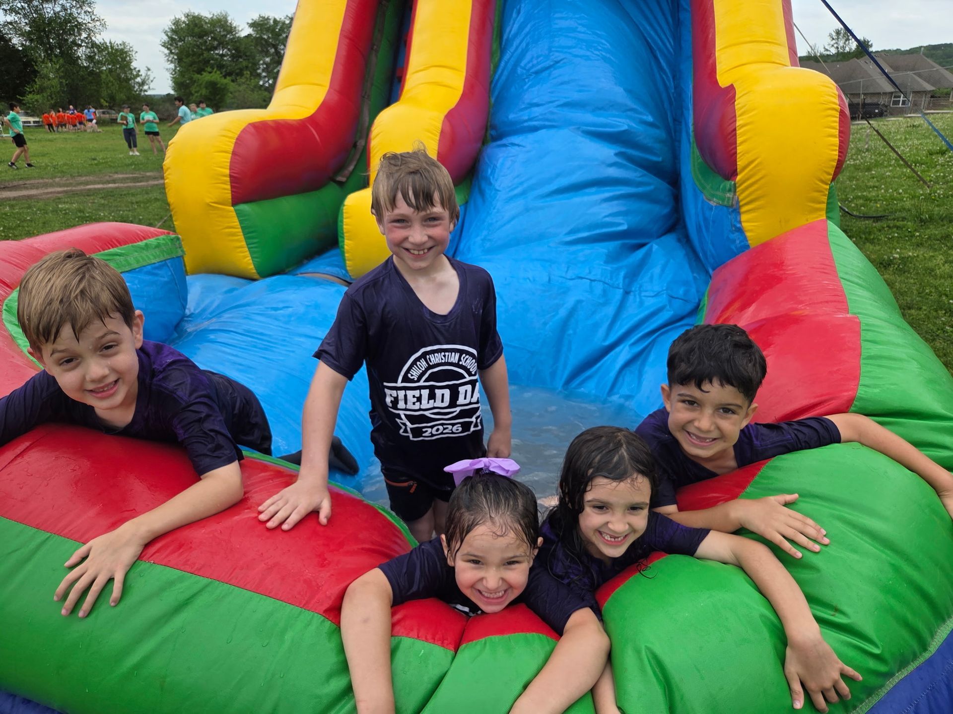 Children smiling on a colorful inflatable slide outdoors.