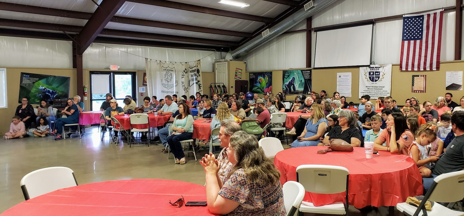 People seated at round tables in a hall with American flag and artwork.